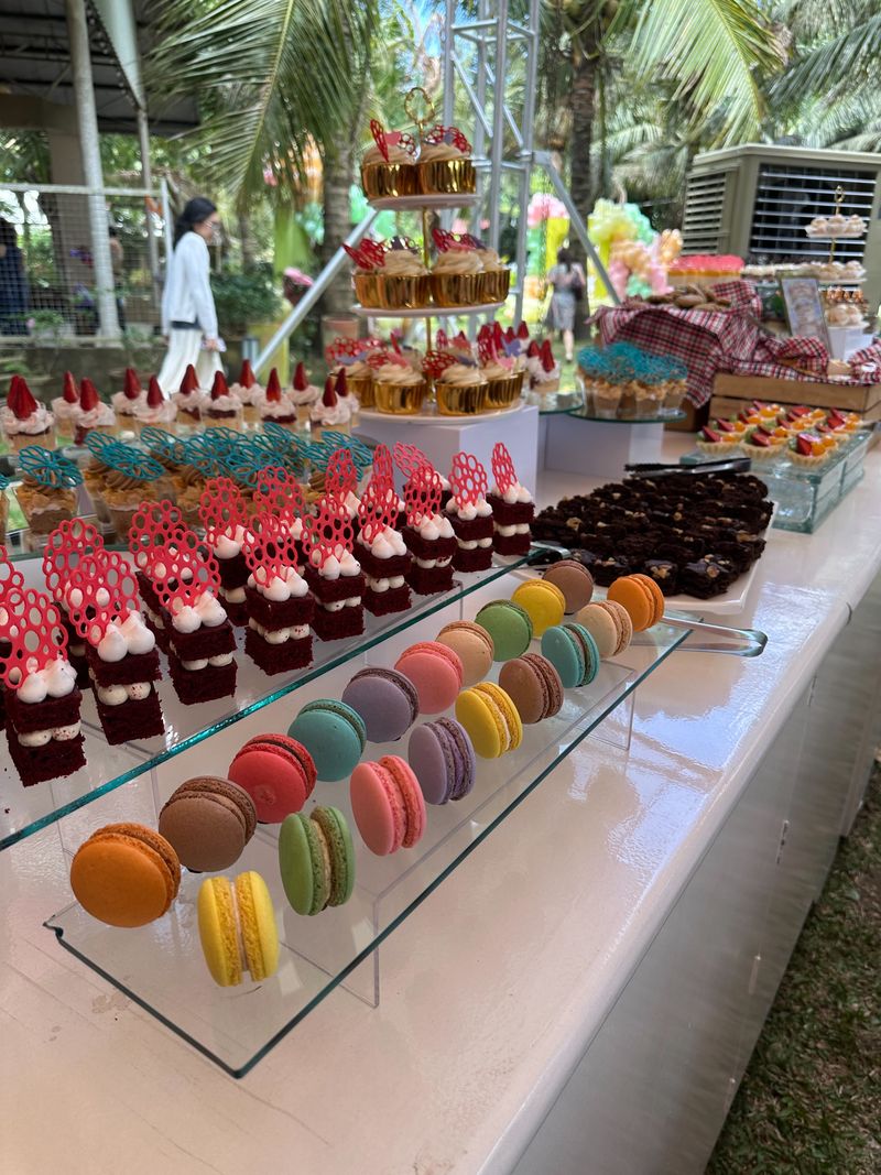 Rows of colorful French macarons on a glass stand beside red layered mini cakes with red lace-style toppers