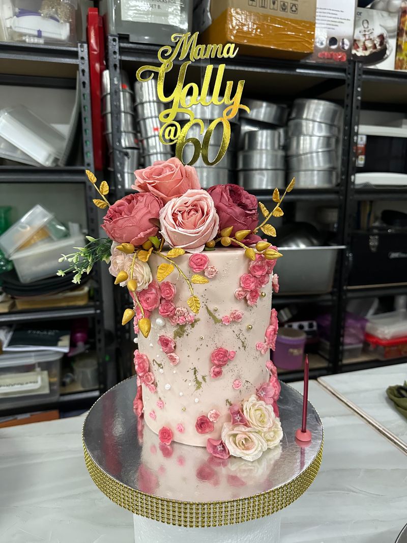 Tall blush-pink 60th birthday cake with roses, gold leaves and a gold script topper