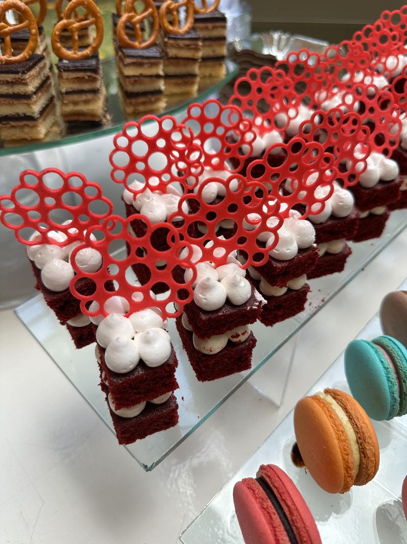 Close-up of red layered mini cakes with piped cream and red lace-style toppers, with macarons alongside